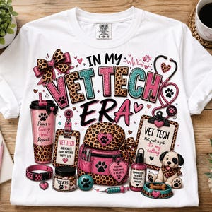 May include: A white t-shirt featuring a graphic print with the text IN MY VET TECH ERA. The design includes a leopard print bow, a pink tumbler, a clipboard labeled VET TECH, a backpack, a treat jar, and a small dog with a leopard print scarf.