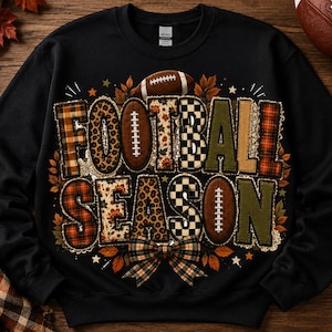 May include: A black crewneck sweatshirt featuring the text FOOTBALL SEASON in large block letters. The letters have varied patterns including plaid, leopard print, and checkered designs. Football graphics and autumn leaves surround the text.