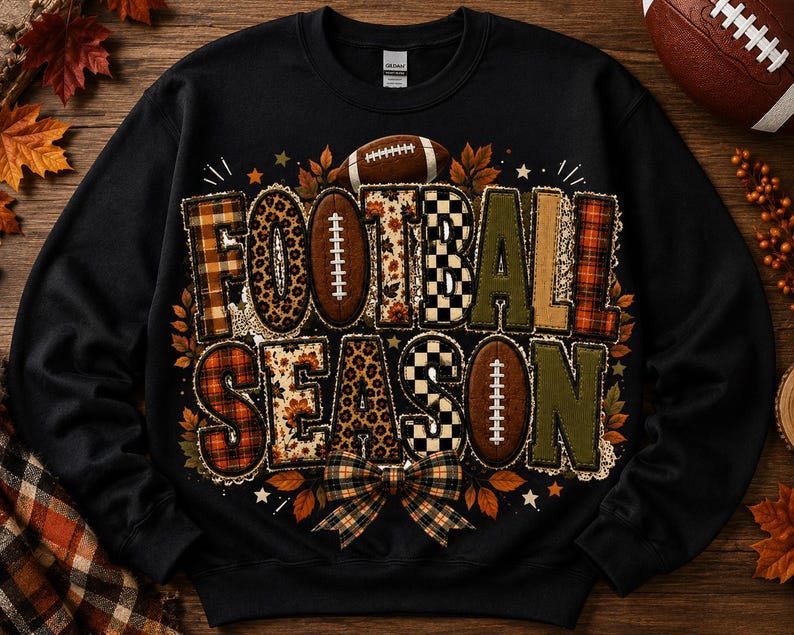 May include: A black crewneck sweatshirt featuring the text FOOTBALL SEASON in large block letters. The letters have varied patterns including plaid, leopard print, and checkered designs. Football graphics and autumn leaves surround the text.