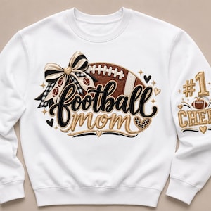 Peut inclure: Un sweat-shirt blanc &agrave; manches longues avec un motif graphique repr&eacute;sentant un ballon de football marron, un n&oelig;ud &agrave; carreaux noir et blanc et le texte football mom. La manche affiche le texte #1 CHEER avec un petit ballon et des d&eacute;tails dor&eacute;s.