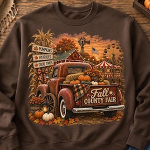 May include: A dark brown crewneck sweatshirt featuring a graphic print of a vintage red pickup truck loaded with pumpkins. The design includes text reading PUMPKINS, HAYRIDES, GOOD TIMES, and FALL COUNTY FAIR, alongside a fairground scene.