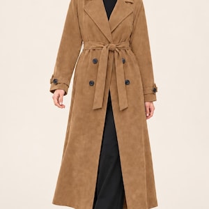 Può includere: Un lungo trench color marrone chiaro, effetto camoscio, caratterizzato da un ampio colletto con risvolti, una cintura da annodare in vita e bottoni neri doppiopetto. Il cappotto presenta maniche lunghe con cinturini ai polsi e taglio lungo.