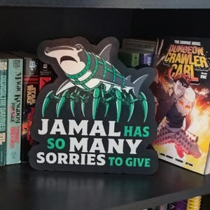 Könnte beinhalten: Ein gestanztes Schild mit einem Cartoon-Hai mit mechanischen Spinnenbeinen in Grau- und Grüntönen. Der Text JAMAL HAS SO MANY SORRIES TO GIVE ist in weißen und grünen Blockbuchstaben auf dem unteren Teil des Schildes aufgedruckt.