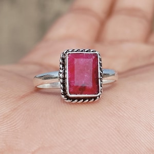 May include: A silver ring featuring a rectangular, deep red gemstone. The gemstone is set within a decorative, twisted rope-like border. The ring's band is a simple, polished silver.