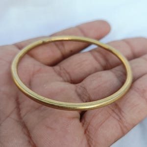 May include: A simple, circular bangle bracelet with a smooth, polished gold-tone finish. The bracelet features a thin, uniform band design that forms a complete, unbroken circle, showcasing a metallic luster and a clean, minimalist aesthetic.