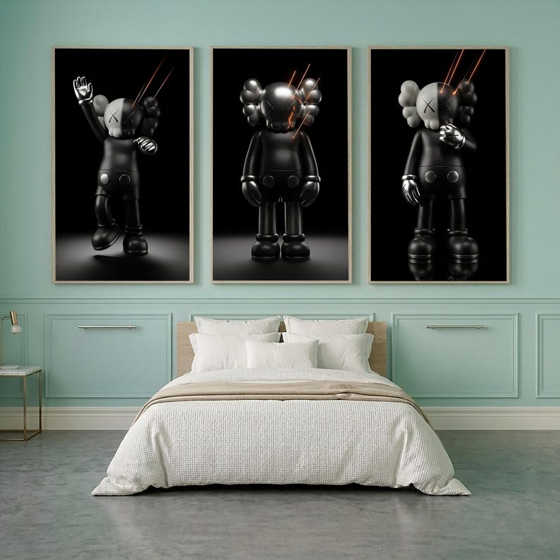 May include: Three framed wall art prints featuring a stylized black and white character with X-shaped eyes. Each print displays the figure in a different pose against a solid black background with thin, glowing orange lines radiating from the head.