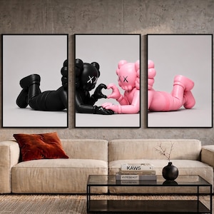 May include: A triptych wall art set featuring three framed prints. The outer prints show a black figure and a pink figure lying down, while the center print shows both figures reaching toward each other to form a heart shape with their hands.