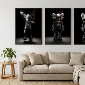May include: Three framed wall art prints featuring black KAWS-style figures against a solid black background. Each figure has signature X-shaped eyes and is depicted with thin red laser-like lines extending from the head area in a dark setting.