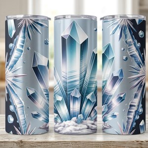 May include: Three stainless steel tumblers with a wraparound design of blue and white crystals. The design features geometric crystal formations and a snowy base, set against a gradient background. Each tumbler is approximately 20 cm tall.