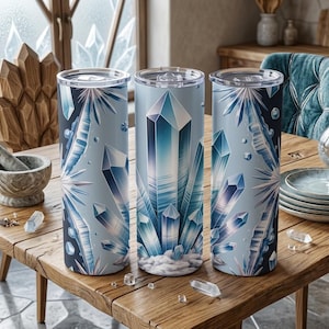 May include: Three cylindrical tumblers with clear lids, decorated with a repeating pattern of blue and white crystals. The tumblers are displayed on a wooden table, with crystal accents and a mortar and pestle in the background.