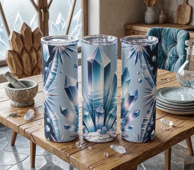 May include: Three cylindrical tumblers with clear lids, decorated with a repeating pattern of blue and white crystals. The tumblers are displayed on a wooden table, with crystal accents and a mortar and pestle in the background.