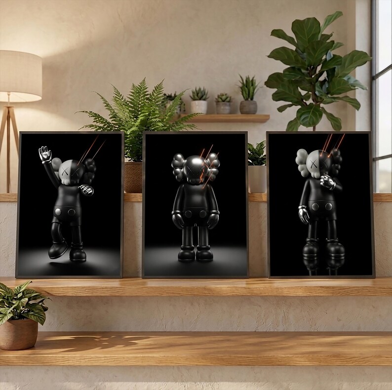 May include: A set of three framed wall art prints featuring a black and white character with X-shaped eyes. Each print displays the figure in a different pose against a solid black background, with thin orange light streaks emanating from the head.
