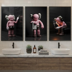 May include: Three framed art prints featuring a pink cartoon figure in a bathroom setting. The figure is depicted in various poses, including showering, holding a towel, and smoking. The bathroom has a white tile wall, a wooden vanity, and two sinks.