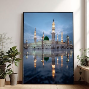 Può includere: Una stampa incorniciata di una moschea con più minareti e una grande cupola verde. L'edificio si riflette nell'acqua sottostante, con un cielo blu sullo sfondo. L'architettura è dettagliata e illuminata.