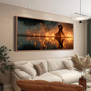 Op de afbeelding: Een ingelijst canvas kunstwerk met een omhelzend stel, afgebeeld tegen een achtergrond van gouden licht en waterreflecties. Het kunstwerk is geplaatst in een donkere, sfeervolle omgeving, met een warm, romantisch thema.