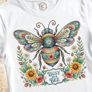 May include: A white t-shirt featuring a large, colorful, intricately patterned bee illustration with teal, orange, and yellow wings. Below the bee are sunflowers, daisies, and red poppies, with the text "BUSY AS A BEE" in a decorative frame.