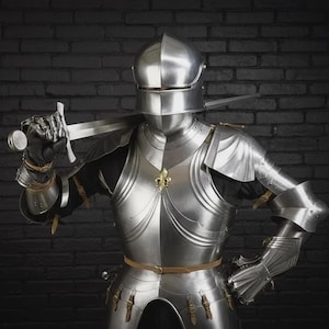Op de afbeelding: Een volledig harnas van gepolijst staal, inclusief helm, borstplaat en gelede ledematen. Het ridderlijke harnas heeft een zwaard over de schouders en een decoratief gouden embleem op de borst. De achtergrond is een donkere bakstenen muur.