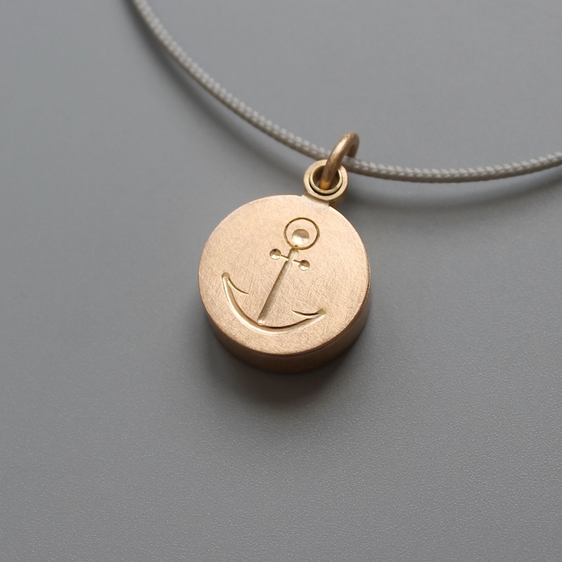 Pu&ograve; includere: Una collana d'oro con un ciondolo rotondo che presenta un design di ancora inciso.