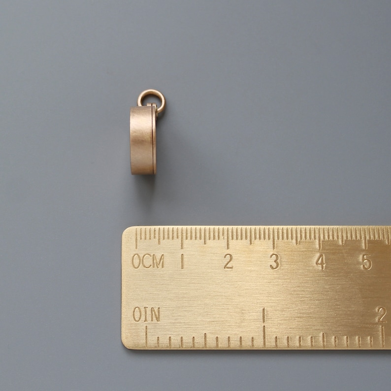 Pu&ograve; includere: Un anello in metallo dorato con un piccolo anello in cima. L'anello ha un diametro di circa 2,5 cm e si trova su una superficie grigia.