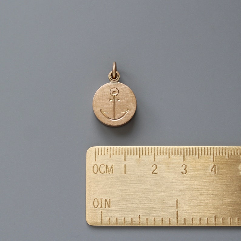 Pu&ograve; includere: Un ciondolo in metallo dorato con un design a forma di ancora. Il ciondolo &egrave; rotondo e ha una superficie liscia. Misura circa 2,5 cm di diametro.