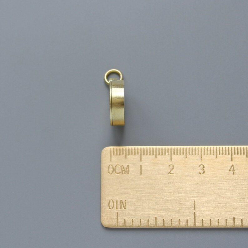 Pu&ograve; includere: Una bussola dorata con un anello in cima. La bussola &egrave; appoggiata su un righello con segni in centimetri.