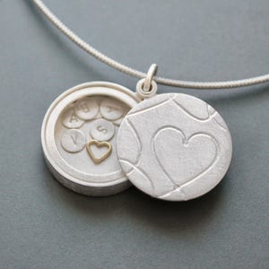 Medallón con mensaje secreto lleno de letras plateadas y un corazón dorado