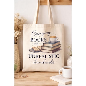 May include: Cream-colored tote bag with the text "Carrying BOOKS and UNREALISTIC standards". The bag features a watercolor illustration of books and a coffee cup. The bag has two handles.