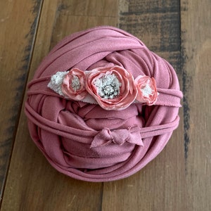 May include: A pink fabric wrap with a pink flower headband. The headband has three pink fabric flowers with white lace and silver glitter accents.