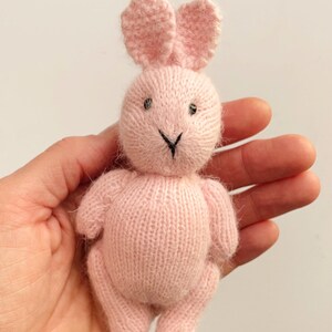 May include: A pink knitted bunny rabbit toy with black embroidered eyes and nose.