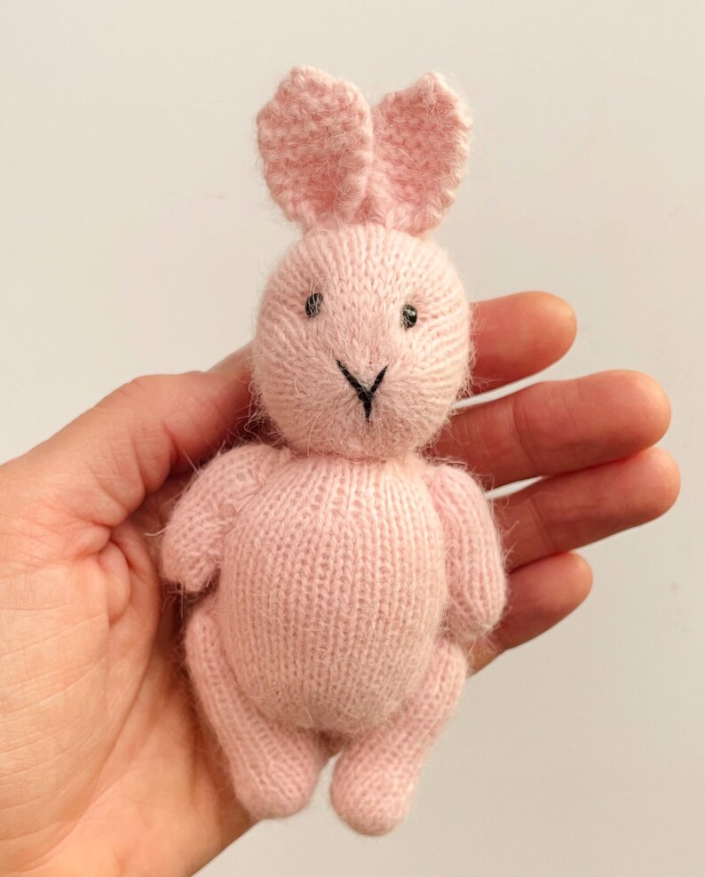 May include: A pink knitted bunny rabbit toy with black embroidered eyes and nose.