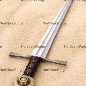 Op de afbeelding: Een metalen zwaard met een tweesnijdend lemmet, een rechte pareerstang en een donkerbruine, met leer omwikkelde greep die is vastgezet met kleine metalen klinknagels. De pommel is een messingkleurige, bloemvormige schijf. De tekst NorthlandForge staat herhaaldelijk afgebeeld.