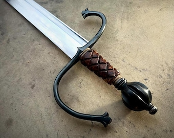 May include: A sword featuring a long, polished steel blade and a dark, curved metal crossguard. The handle is crafted from a textured, reddish-brown material with a diamond-patterned grip, ending in a rounded, dark metal pommel at the base.