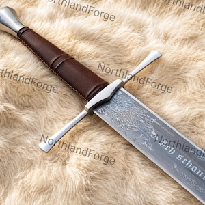 May include: A metal sword with a brown leather-wrapped grip, a silver pommel, and a crossguard. The blade features an intricate etched design of a wolf and the text "noch schone niema" engraved along the flat surface of the steel blade.