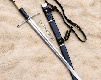May include: A steel longsword with a dark blue leather-wrapped grip, a cream-colored corded handle section, and a silver pommel. Beside it lies a matching dark blue leather scabbard with black leather straps and brass buckles, marked NorthlandForge.