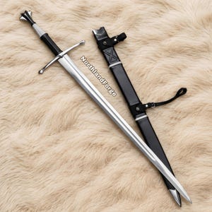Peut inclure: Une épée en acier argenté avec une poignée gainée de cuir noir, une garde en croix et un pommeau. À côté se trouve un fourreau en cuir noir avec des accents en métal argenté et une sangle noire. Le texte NorthlandForge est visible sur la lame.