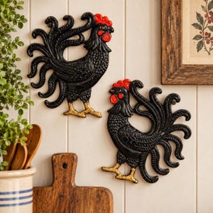 May include: Two black rooster wall decorations featuring textured feathers, bright red combs and wattles, and gold-painted feet. These wall-mounted figures display intricate scrollwork in the tail feathers and are positioned facing each other.