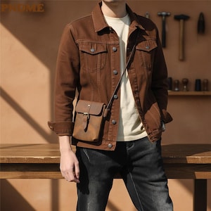 May include: A brown denim jacket with a pointed collar, button-front closure, and two chest pockets, worn over a plain cream t-shirt. A small, rectangular brown leather crossbody bag with a buckle strap hangs across the torso.