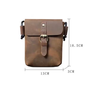 May include: A brown leather crossbody bag with a front flap, a metal buckle closure, and black side cord attachments. The bag measures 18.5 cm in height, 13 cm in width, and 3 cm in depth as indicated by the visible measurement lines.