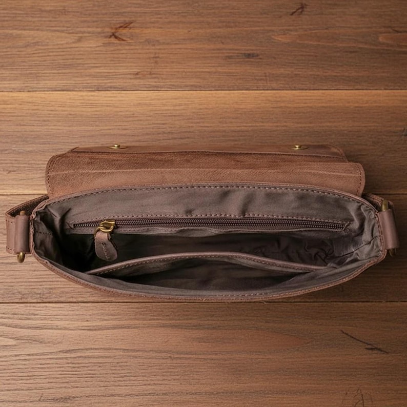 Peut inclure: Sac messager en cuir marron ouvert, r&eacute;v&eacute;lant l'int&eacute;rieur. Le sac est dot&eacute; d'un rabat, d'un compartiment principal zipp&eacute; et d'une poche interne. Le cuir pr&eacute;sente une finition vieillie.