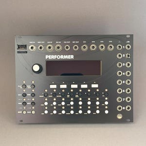 May include: Black electronic music device with the word "PERFORMER" above a screen. It has numerous buttons, knobs, and input/output jacks. The device is designed for music production and performance.
