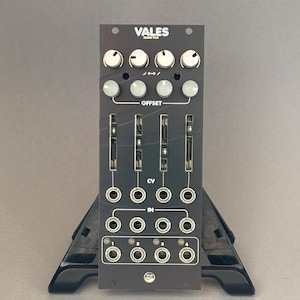 May include: Black electronic music synthesizer module with the text "VALES QUAD VCA". It features knobs, sliders, and input/output jacks. The module is mounted on a black stand.