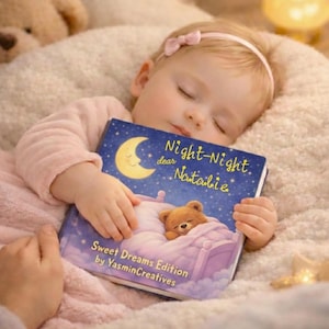 Puede incluir: Un bebé dormido con un mono rosa sostiene un libro infantil titulado "Night-Night dear Natalie". La portada del libro presenta una luna creciente, estrellas y un oso de peluche en una cama. También se ven las palabras "Sweet Dreams Edition".