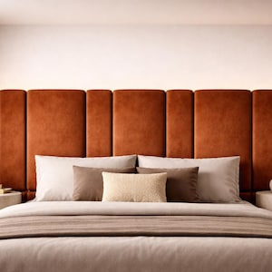 May include: A tall, rectangular, rust-colored velvet upholstered headboard featuring vertical channel tufting. The headboard spans the width of the bed, which is dressed in layered beige and brown bedding, including two large pillows and a central textured cushion.
