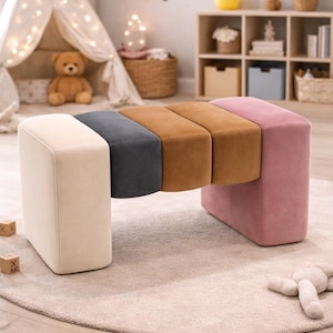 Puede incluir: Un banco moderno multicolor con un diseño único. El banco presenta un extremo color crema, seguido de una sección gris oscuro, dos secciones marrones y un extremo rosa. El banco está colocado sobre una alfombra de color claro en una habitación infantil.