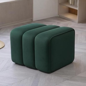 Puede incluir: Un otomán verde oscuro de tres secciones con bordes redondeados. La pieza tapizada tiene un diseño moderno y es adecuada para una sala de estar o un salón. El otomán es de color liso y tiene una textura suave y aterciopelada.