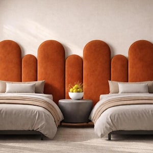 Op de afbeelding: Twee bedden met bijpassende oranje hoofdborden. Elk bed heeft een lichtgekleurd dekbed en kussens. Tussen de bedden staat een kleine grijze tafel met een fruitschaal. De hoofdborden hebben een boogontwerp.