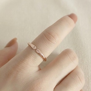 May include: A rose gold-toned open ring featuring two tapered ends, each engraved with a single letter. One end displays the letter S, while the other end displays the letter H. The band has a smooth, polished finish and an adjustable open design.