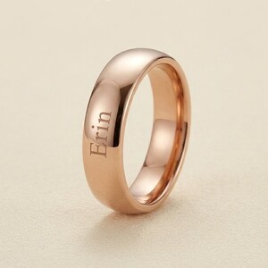 Peut inclure: Une bague en or rose avec le nom "Erin" gravé à l'extérieur. La bague a une surface lisse et polie et une forme arrondie. La bague est de conception simple.