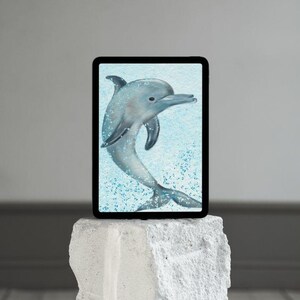May include: A digital tablet displays a watercolor illustration of a dolphin. The dolphin is gray with a curved body, fins, and a long snout, set against a light blue background with water droplets. The tablet rests on a white, textured pedestal.