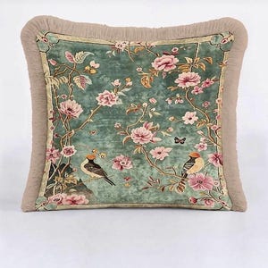 May include: Square decorative pillow with a teal background featuring a floral design with pink flowers, birds, and butterflies. The pillow has a fringed border in a neutral beige color.